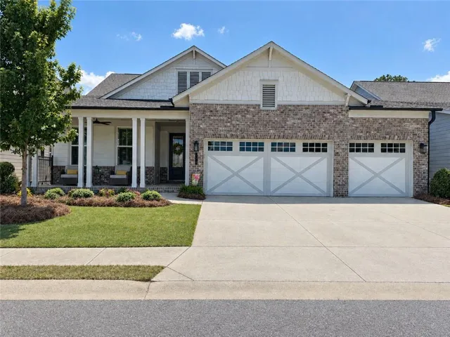 Brick and siding exterior featuring a covered front porch, dual garage doors with window accents, and a concrete driveway