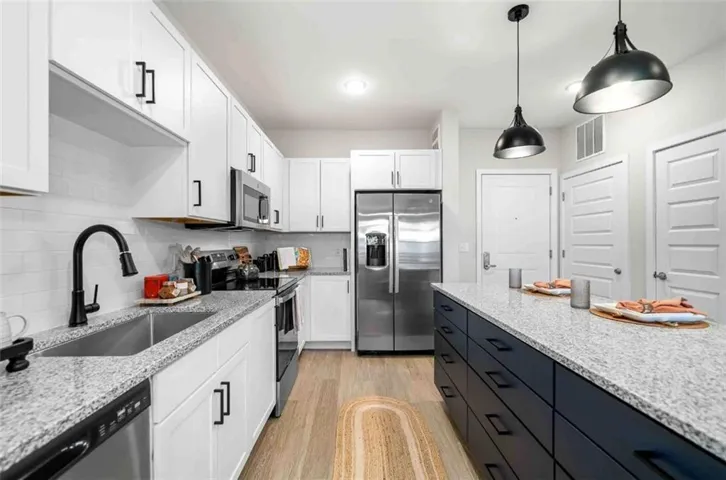 Kitchen with appliances with stainless steel finishes, light stone counters, decorative light fixtures, and white cabinets