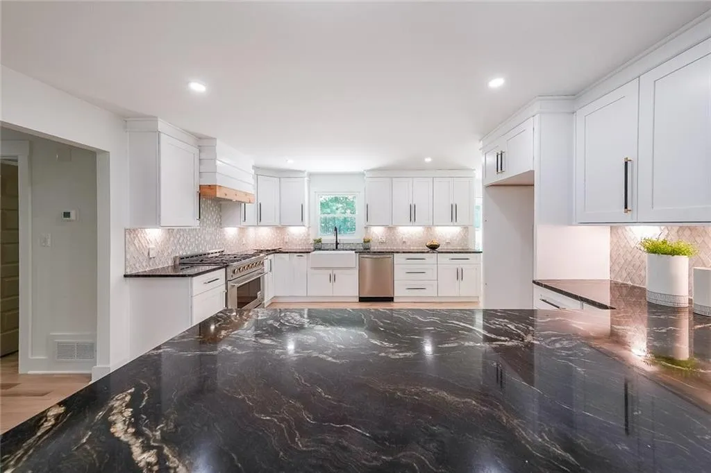 Kitchen featuring white cabinetry, stainless steel appliances, dark stone countertops, light hardwood / wood-style floors, and backsplash