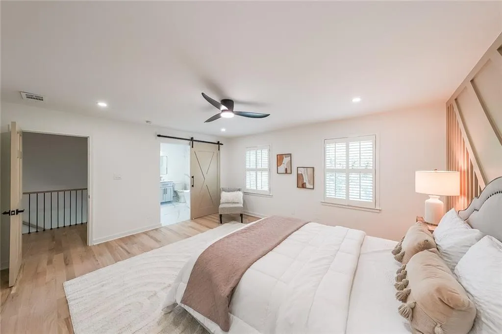 Bedroom featuring ensuite bathroom, light hardwood / wood-style flooring, a barn door, and ceiling fan