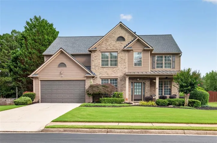Traditional-style residence featuring a brick and siding facade, covered front porch, and a two-car garage