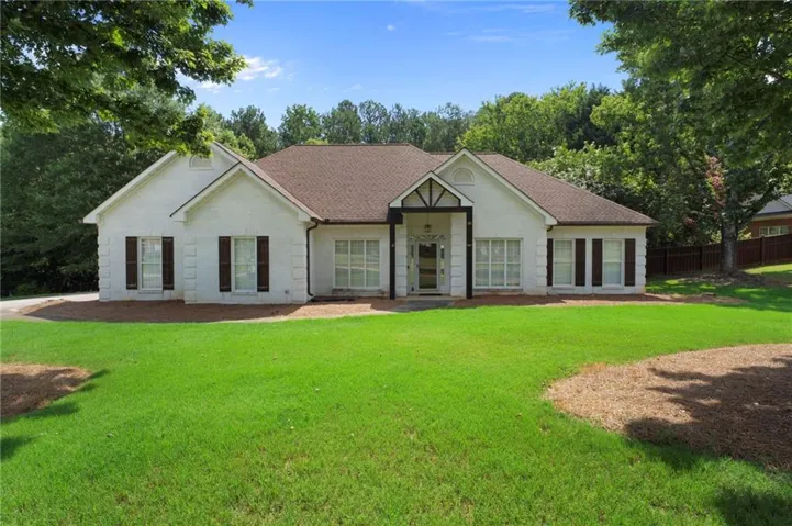White brick exterior featuring a covered entry, dark brown shutters, a gabled roofline, and an expansive front lawn