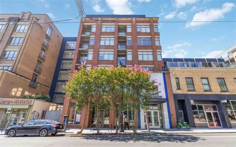 Multi-story building featuring a brick facade, multiple balconies, large windows, and ground-level retail spaces
