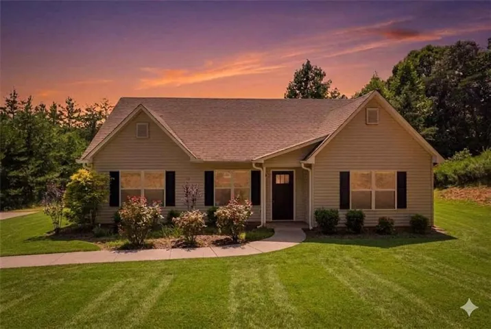Beige siding exterior with dark shutters, dark front door with glass panel, and gabled roofline. Grass is digitally enhanced to give the buyer an idea of green grass.
