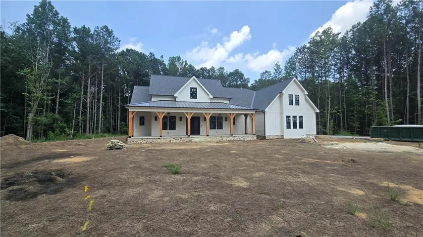 Modern farmhouse exterior with a dark gray shingle roof, white board and batten siding, dark framed windows, and a covered front porch with exposed timber columns