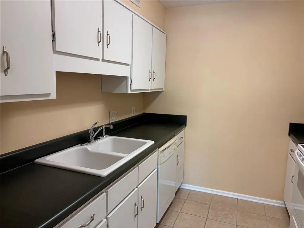 Kitchen featuring white cabinetry, dark countertops, white appliances, and light tile patterned flooring