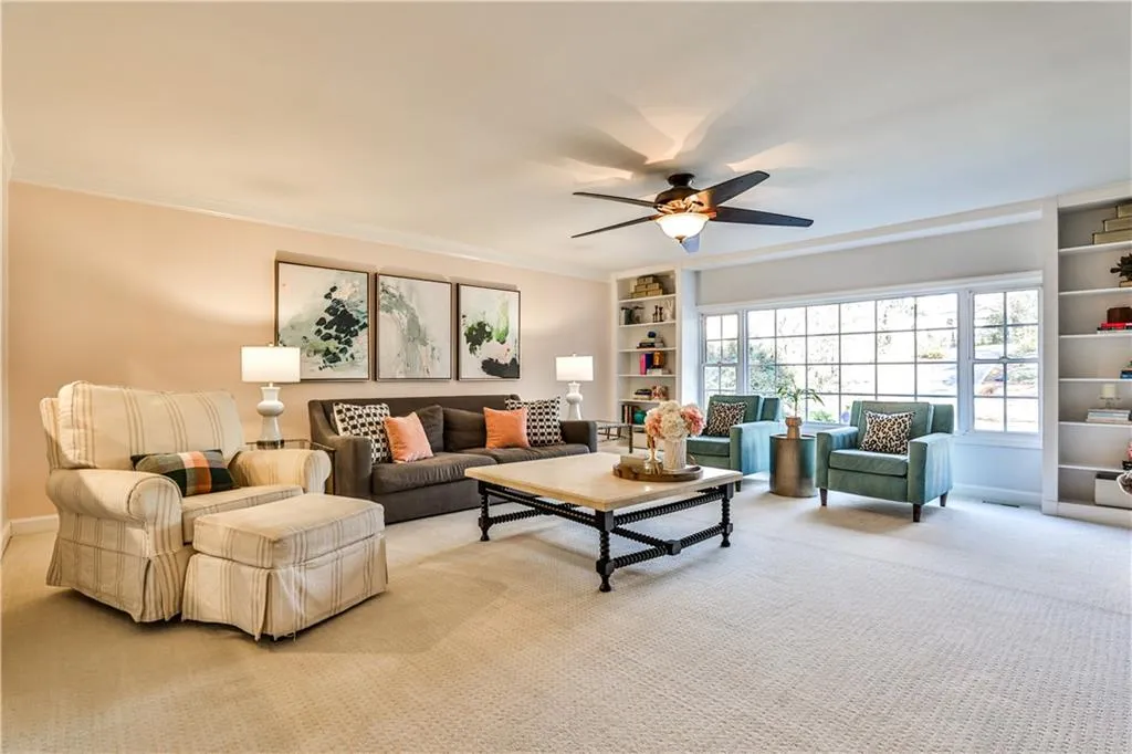 Living room featuring built in features, carpet floors, ornamental molding, and ceiling fan