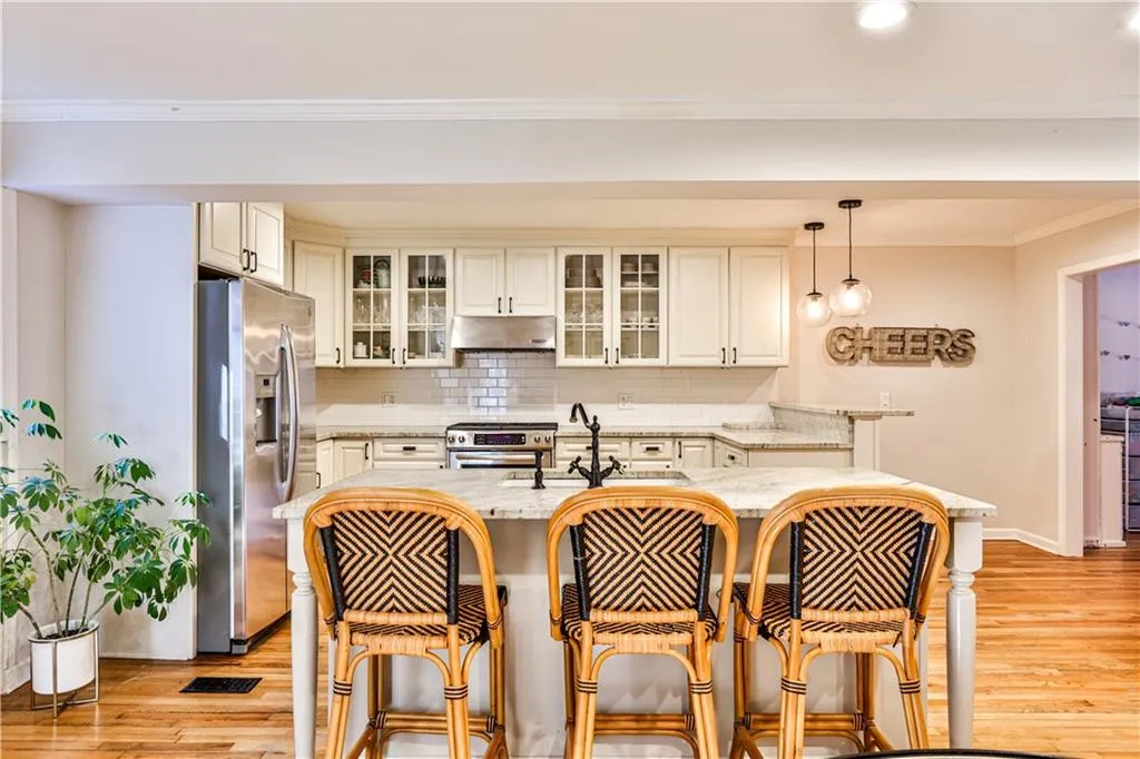 Kitchen featuring a breakfast bar area, light stone counters, crown molding, hanging light fixtures, and appliances with stainless steel finishes