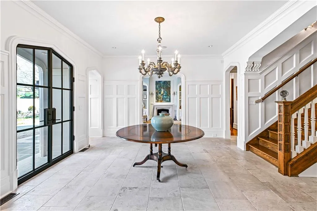 Foyer entrance featuring crown molding, arched front door, chandelier, diamond-paned leaded glass windows,  and a wainscoted wall