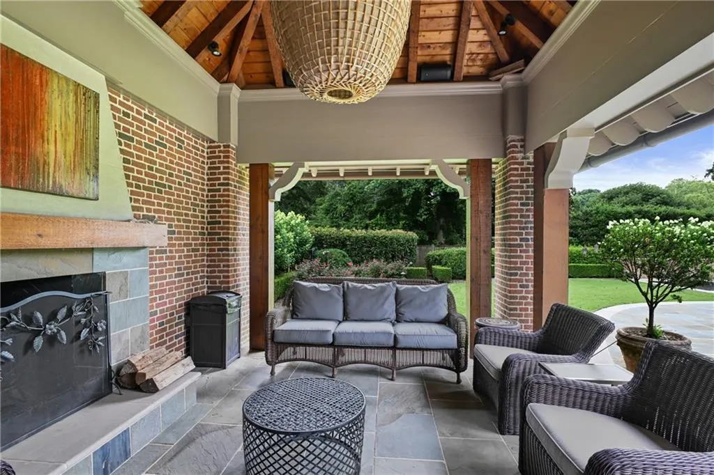 Covered outdoor living space featuring a wood-beamed vaulted ceiling, a brick fireplace with stone surround and hearth, and slate tile flooring