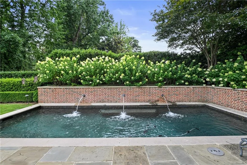Plunge pool featuring three water jets, a surrounding brick wall, and lush flowering shrubs