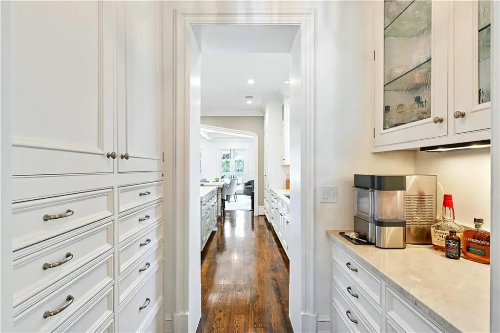 Butler's pantry with stone countertops, white cabinetry, crown molding, glass insert cabinetry