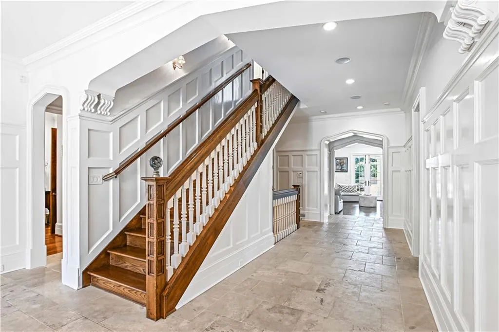 Staircase featuring arched walkways, crown molding, a decorative wall, stone tile floors, and recessed lighting