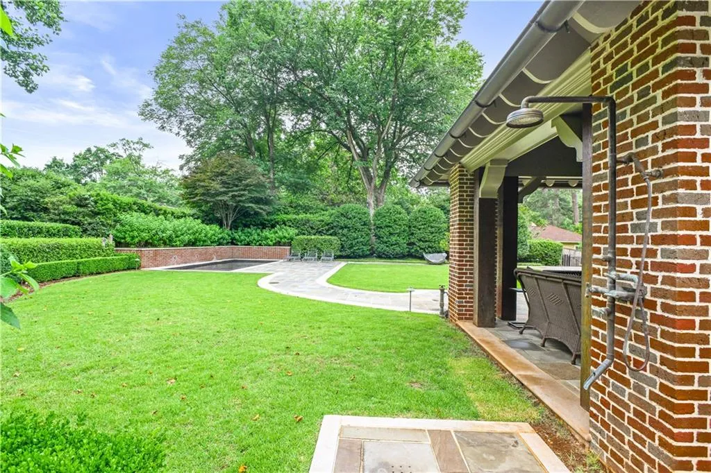 Expansive backyard featuring a manicured lawn, an outdoor shower, and a covered patio with exposed beams