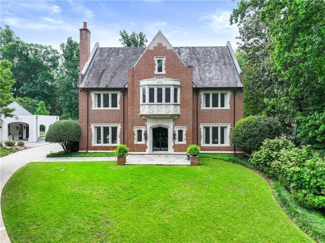 Brick facade residence featuring a prominent bay window with ornate detailing, multiple casement windows, a slate-style roof, and a paved drive