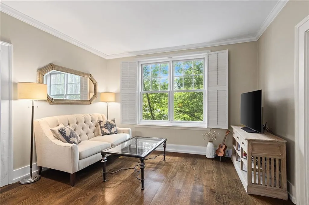 Hardwood flooring paired with crown molding and a large window featuring interior shutters