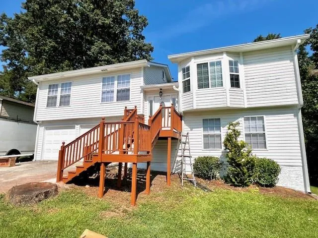 White siding exterior featuring a multi-level deck with wood railings, bay window, and a two-car garage