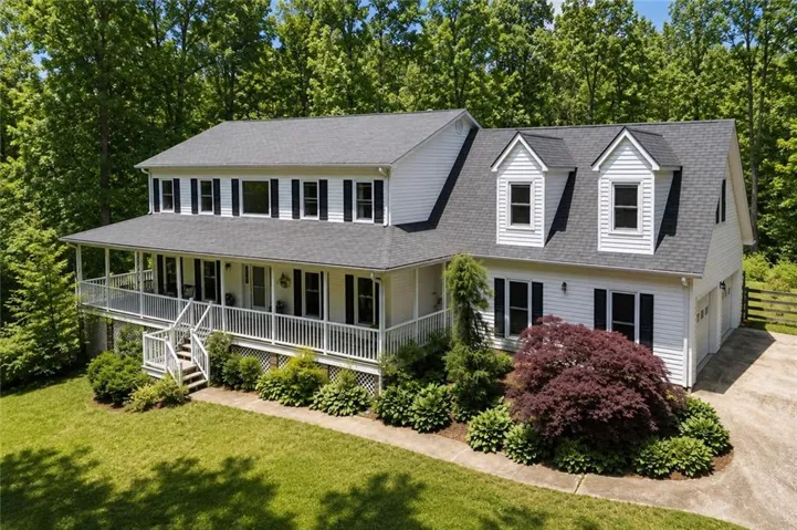 Two-story home featuring a full-width front porch with white railings, dormer windows, and a two-car garage