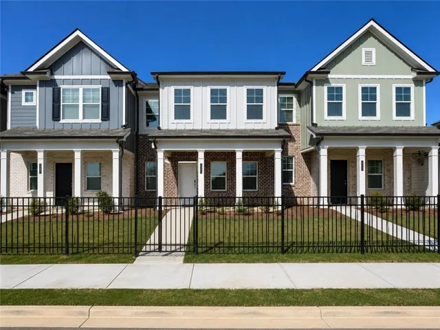 Modern townhome exterior featuring mixed material siding, brick accents, white columns, and a black wrought iron fence