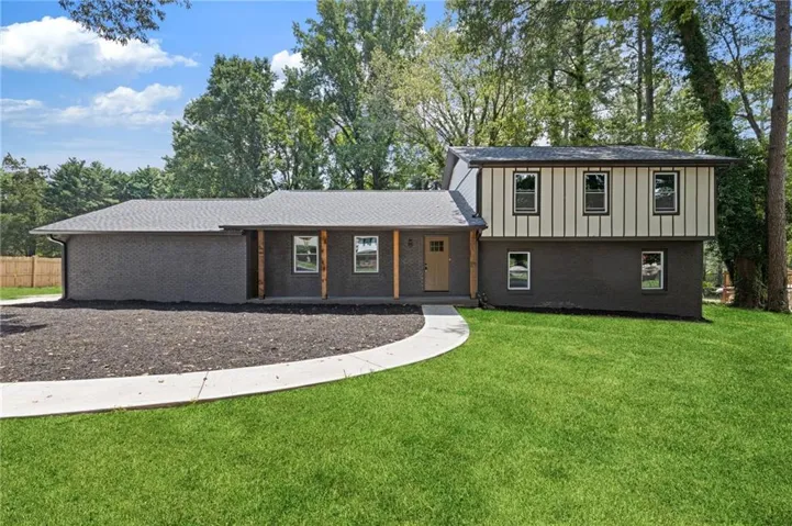 Two-story exterior with dark brick and vertical panel siding, wood-wrapped columns, and a light-colored front door