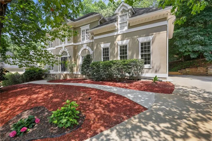 Stucco exterior with architectural accents, multiple windows with white trim, a paved driveway, and established landscaping