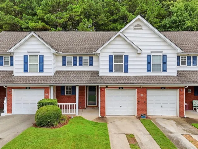 Townhome exterior featuring white siding, a shingle roof, and red brick accents