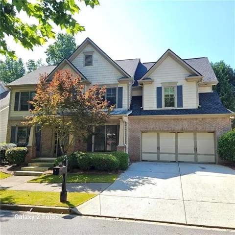 Two-story residence featuring a brick and siding exterior, a two-car garage, and mature landscaping