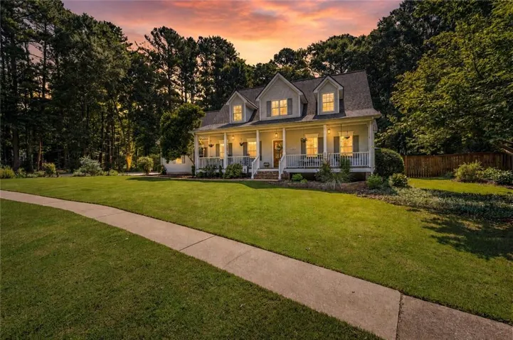 Gable-front home featuring a full-width covered porch with white railings, dormer windows, and a dark shingle roof