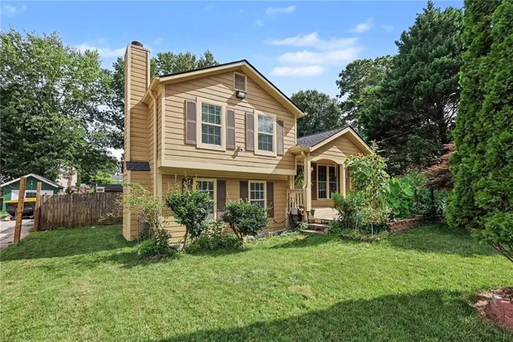 Exterior featuring beige siding, dark brown shutters, a prominent chimney structure, a covered front entry with steps, and a landscaped front yard with established greenery