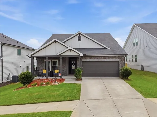 Cottage-style residence featuring a stone and siding exterior, an attached two-car garage, and a covered front porch