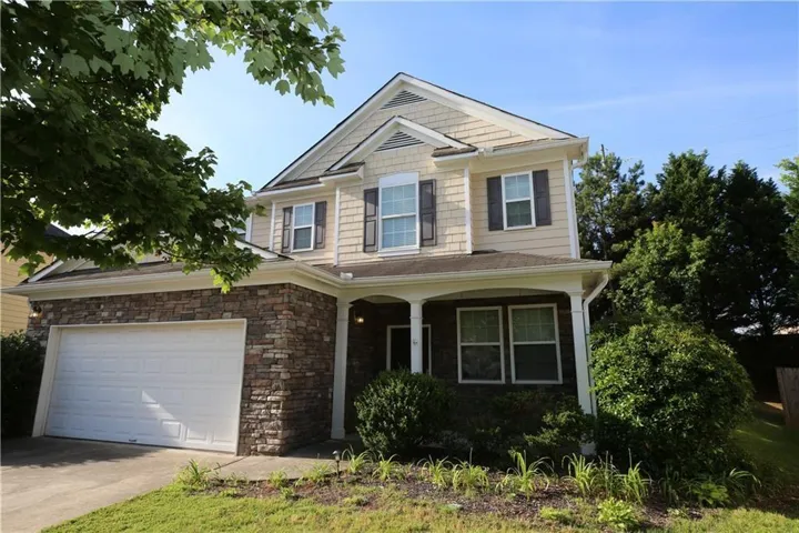 Two-story residence featuring a stone and siding facade, a covered front porch, and an attached two-car garage