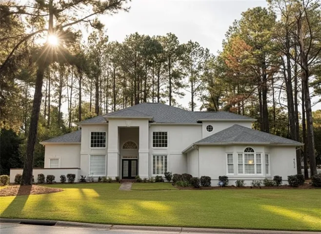 View of front facade featuring a front lawn, stucco siding, roof with shingles, and view of scattered trees