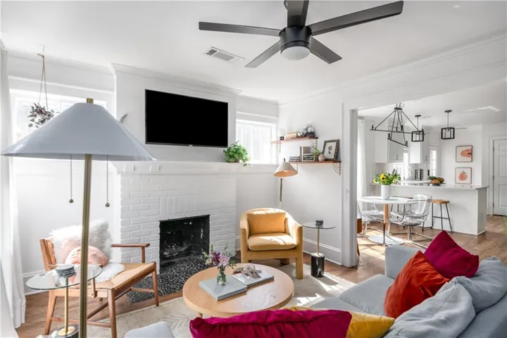 Living room with wood finished floors, a chandelier, a brick fireplace, and crown molding
