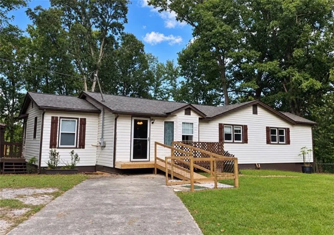 White siding exterior with brown shutters, dark-toned roof, front entry ramp, and an additional side deck