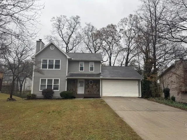Grey siding exterior with a prominent chimney, an attached garage, a covered front porch, and a paved driveway