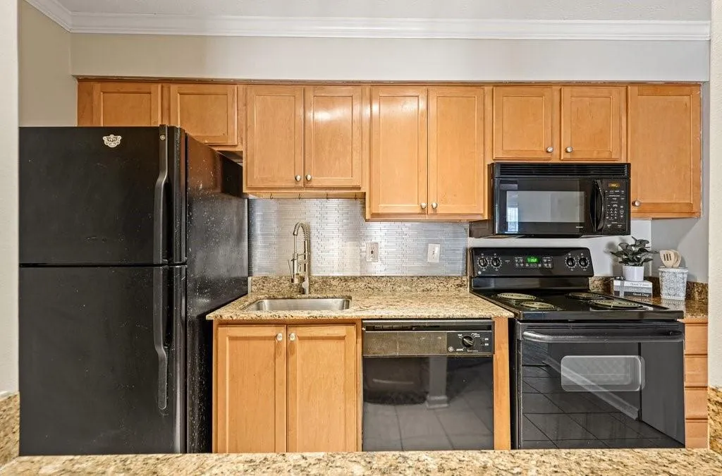 Kitchen featuring light-finish cabinetry, stone-surface countertops, a metallic-finish backsplash, and a suite of black appliances including a built-in microwave and dishwasher