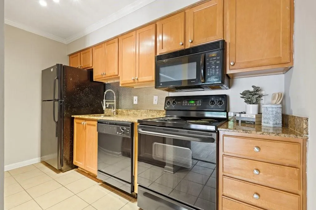 NOT STAGED Kitchen featuring shaker-style wood cabinetry, stone countertops, tiled flooring, and a suite of black appliances including a built-in microwave, range, dishwasher, and refrigerator