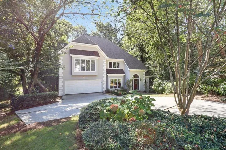 Stucco exterior with a dark shingle roof, arched entryway, bay window, and a two-car garage