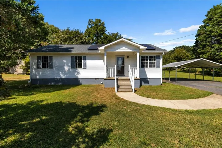 White siding exterior with a covered front porch, concrete walkway, attached carport, and solar panels