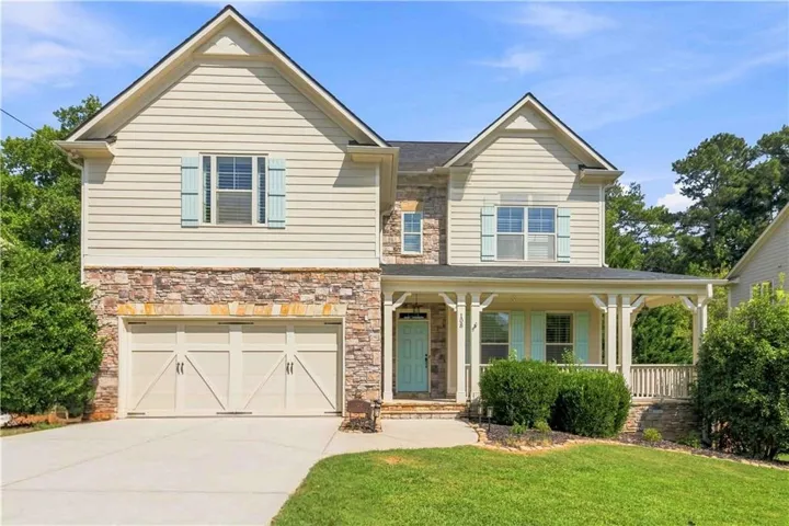Two-story exterior with stone and siding facade, covered front porch, attached two-car garage, and established landscaping