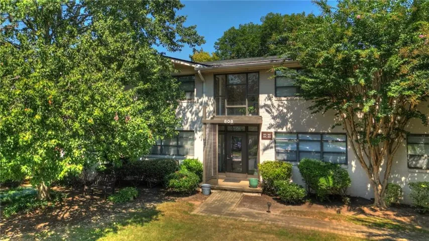 Two-story exterior with a brick facade and multiple windows, featuring mature trees and established landscaping
