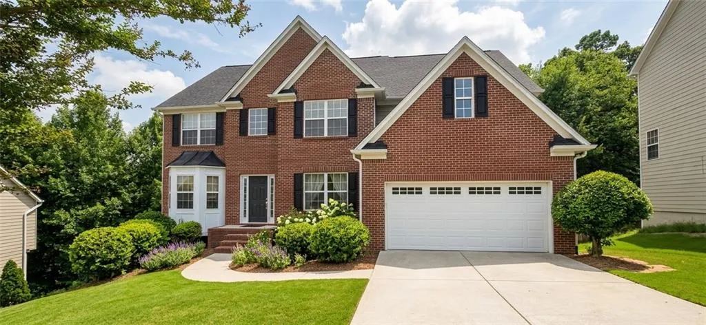 Brick exterior with a peaked roofline, a two-car garage, a concrete driveway, and a front entry with a bay window