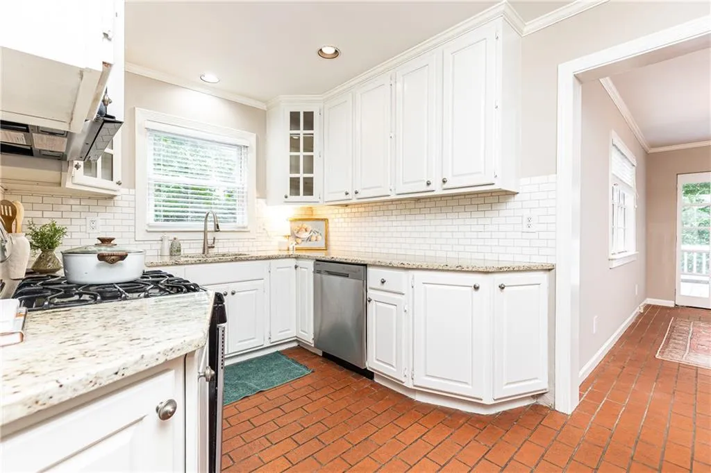 Kitchen with brick flooring, decorative backsplash, white cabinetry, ornamental molding, and stainless steel appliances