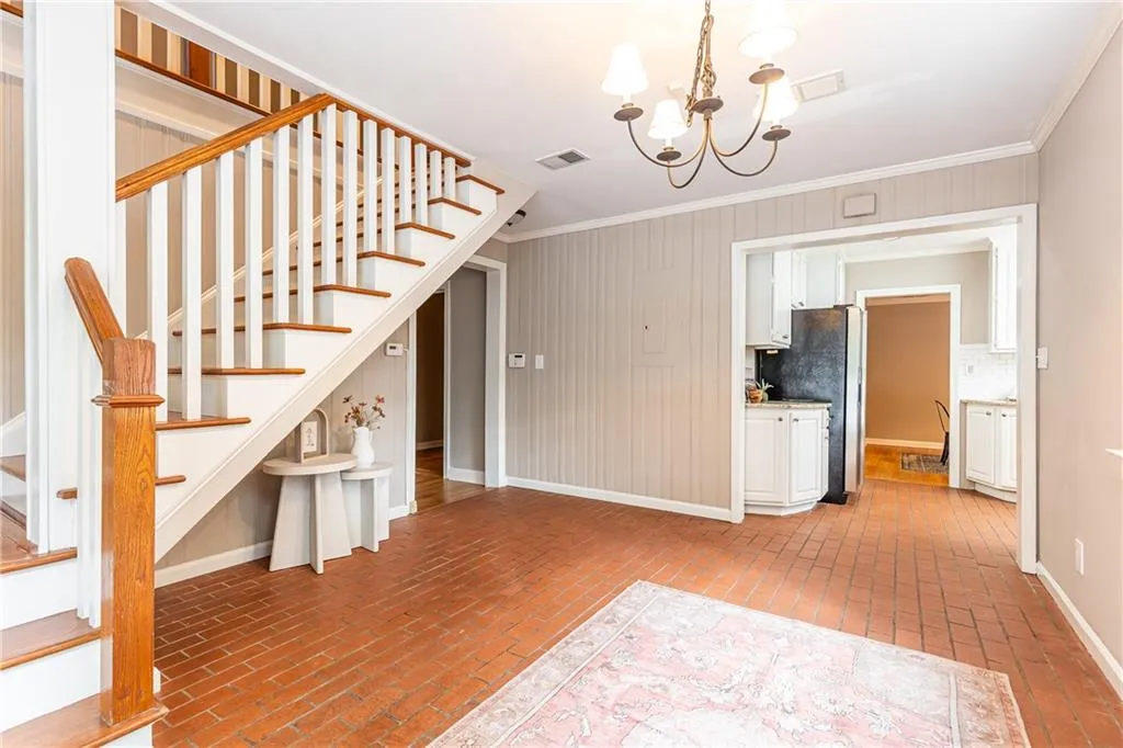 Stairway with crown molding, a chandelier, brick floors, and wood walls