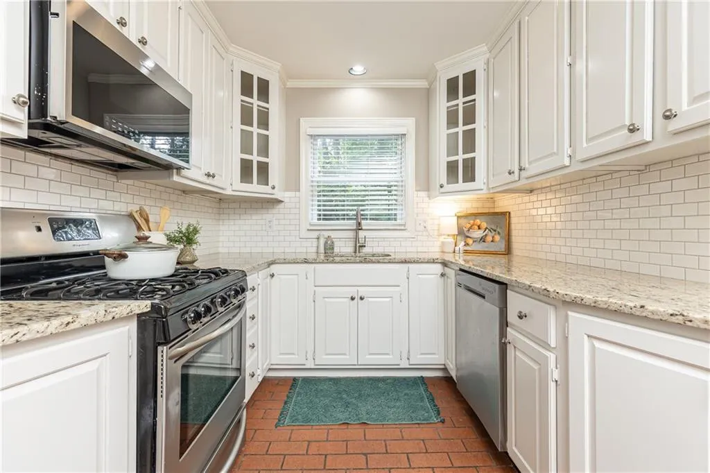 Kitchen with stainless steel appliances, decorative backsplash, white cabinets, light stone counters, and glass insert cabinets