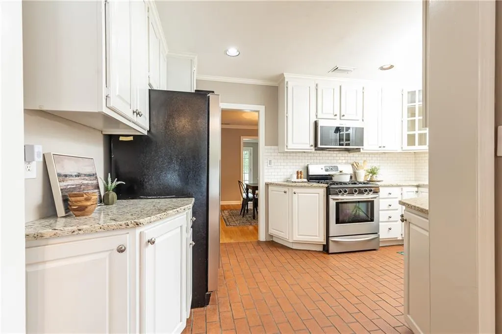 Kitchen with ornamental molding, appliances with stainless steel finishes, brick floors, white cabinetry, and tasteful backsplash