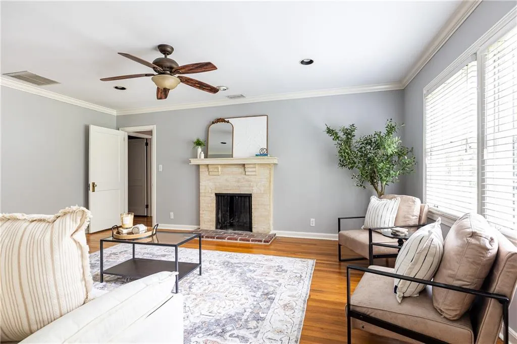 Living area featuring ornamental molding, a fireplace with raised hearth, wood finished floors, and a ceiling fan