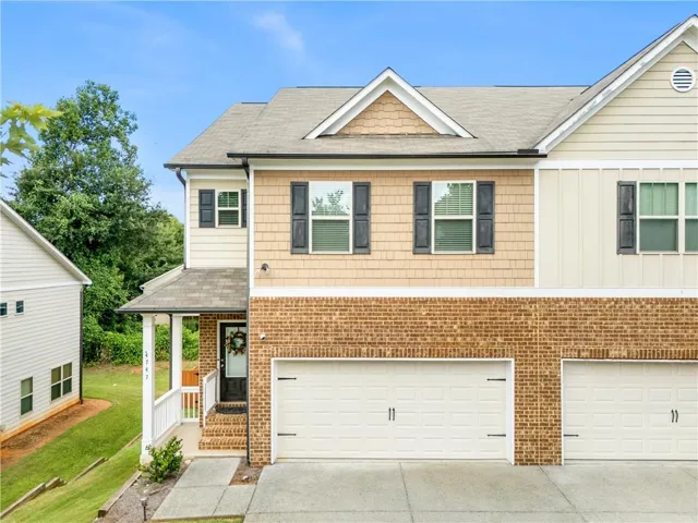 Brick and siding exterior featuring a covered front porch, white railings, and a two-car garage