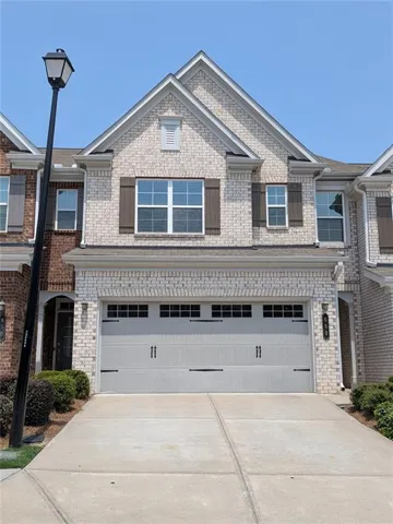 Brick facade townhouse featuring a two-car garage, concrete driveway, and gabled roofline