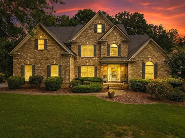 Brick and stone veneer exterior with dark shutters, multiple gables, an arched entryway, and a mature landscaped lawn